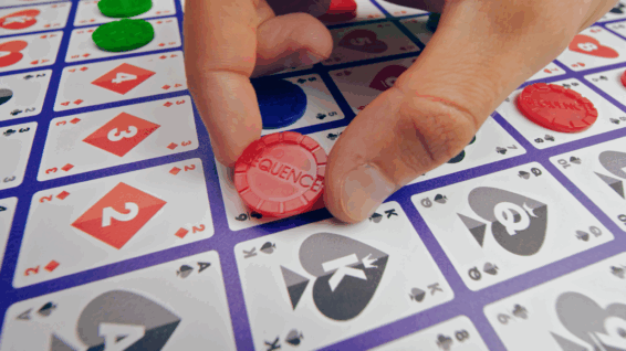 een persoon die een fiche neerlegd op het speelbord van het spel Sequence Classic